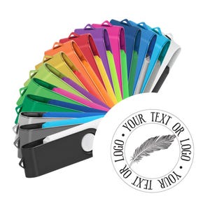 May include: A selection of multi-coloured USB flash drives, fanned out to display a range of colours. Each drive has a white button and a black or silver casing. A white circle displays the text "YOUR TEXT OR LOGO" around a feather illustration.