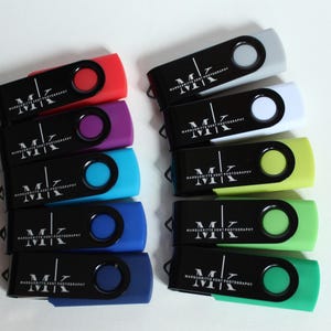 Puede incluir: Una colecci&oacute;n de memorias USB de colores. Cada unidad tiene un cuerpo negro con un bot&oacute;n circular de color y un acento de color a juego. Las unidades est&aacute;n etiquetadas con el texto "MK MARGUERITTE KENT PHOTOGRAPHY" en blanco.