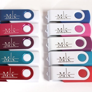 Puede incluir: Una colecci&oacute;n de unidades flash USB en varios colores, incluyendo azul, rosa, morado, turquesa y rojo. Cada unidad tiene un cuerpo blanco y un extremo giratorio de color. Las unidades est&aacute;n marcadas con el texto "MK MARGUERITTE KENT PHOTOGRAPHY marguerittekent@hotmail.com".