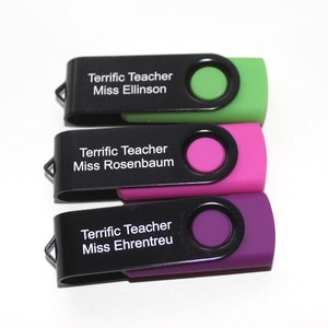 Puede incluir: Tres memorias USB con tapas giratorias negras y detalles de colores. Cada unidad est&aacute; etiquetada como "Terrific Teacher" seguida del nombre de una profesora: Miss Ellinson, Miss Rosenbaum y Miss Ehrentreu. Los detalles son verdes, rosas y morados.