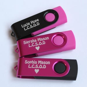 Puede incluir: Tres unidades flash USB en negro y rosa. Cada unidad tiene un dise&ntilde;o giratorio y presenta un nombre e iniciales en texto blanco. Dos unidades son rosas con un bot&oacute;n rosa y una es negra con un bot&oacute;n rosa.