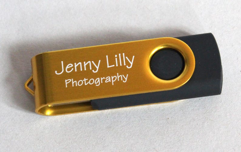 Puede incluir: Una unidad flash USB dorada y negra. La parte dorada tiene el texto "Jenny Lilly Photography" en blanco. La unidad USB tiene un dise&ntilde;o giratorio y un peque&ntilde;o lazo para sujetarla a un llavero.