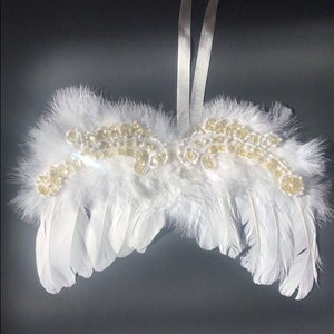 May include: White feather angel wings with gold beaded accents and a white satin ribbon for hanging.