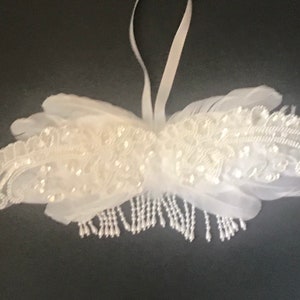 May include: White feather wings with beaded embellishments and a pearl drop fringe. The wings are attached to a white ribbon.