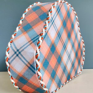 May include: A heart-shaped box with a plaid pattern in shades of blue, white, and peach. The box has a white and orange trim around the edges.
