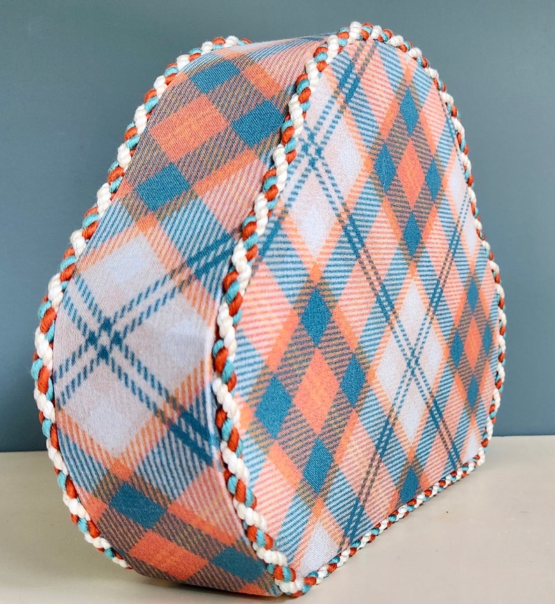 May include: A heart-shaped box with a plaid pattern in shades of blue, white, and peach. The box has a white and orange trim around the edges.