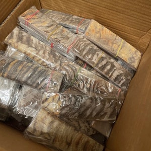 May include: A cardboard box filled with numerous pieces of petrified wood, each wrapped in clear plastic and secured with rubber bands. The wood has a distinctive brown and white striped pattern.
