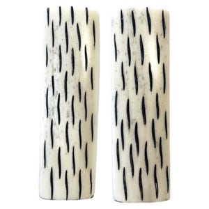 May include: Two white bone knife handles with black markings. The handles have a natural, organic look.