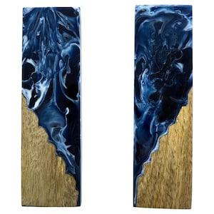 May include: Two rectangular wooden blocks with a gold finish on the bottom half and a swirling blue and white resin design on the top half. The resin has a marbled effect, creating a unique pattern on each block.