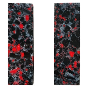 May include: Two rectangular blocks featuring a composite material with a speckled pattern. The surface displays a mix of black, bright red, and translucent grey fragments embedded within a dark base, creating a high-contrast, multi-colored texture.