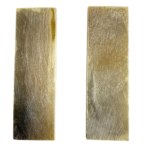 May include: Two rectangular pieces of light brown material with a textured, scratched surface. The pieces are side by side against a white background. The material has a slight yellow hue in some areas.