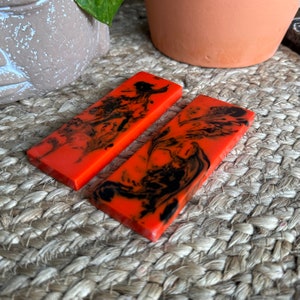 May include: Two orange and black resin blanks with a marbled pattern. The blanks are rectangular and have a smooth, glossy finish.