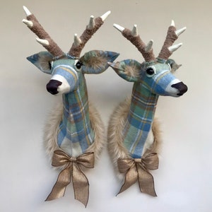 May include: Two decorative deer heads made of fabric with a plaid pattern in shades of blue, green, and white. Each head has a faux fur collar and a gold bow.