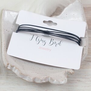 May include: A black cord bracelet on a white card with the text "Flying Bird Jewelry".