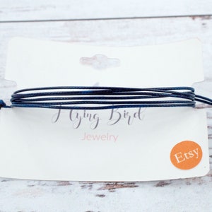 May include: A dark blue cord bracelet on a white card with the text "Flying Bird Jewelry" and a small orange circle with the text "Etsy".