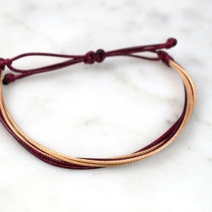 May include: A burgundy and gold braided cord bracelet with a simple knot closure.