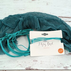 May include: A set of teal blue cord bracelets with a white card that says "Flying Bird Jewelry" and a small orange circle with the word "Etsy" on it. The bracelets are wrapped in a teal blue fabric.