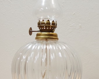 May include: A clear glass oil lamp with a ribbed body and a brass top. The lamp has a round shape and a wick.