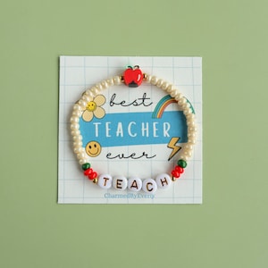 May include: A bracelet with the word "TEACH" spelled out in white letter beads. The bracelet is on a card that says "best TEACHER ever" with a flower, rainbow, and lightning bolt graphic. An apple bead tops the bracelet.