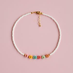 May include: A white beaded necklace with a gold clasp and colourful letter beads spelling out the name "EVERLY".