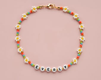 May include: A colorful beaded necklace with white daisy beads and the name "EVERLY" spelled out in white beads with black lettering.