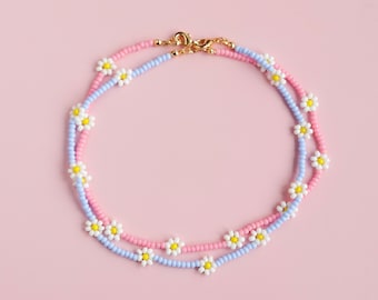 May include: A delicate double-strand necklace with pink and light blue beads, featuring small white daisy-shaped charms.