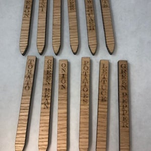 May include: Set of 12 wooden plant markers with different vegetable names written on them. The markers are all the same size and shape, and they are made of natural wood.