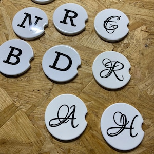May include: Set of 8 white round coasters with black letter initials A, B, C, D, E, H, N, and R. The coasters are made of a hard, durable material and are perfect for protecting surfaces from spills and scratches.