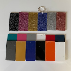 May include: Assortment of 15 blank keychains in various colors, including black, pink, gold, blue, gray, teal, red, white, and orange. The keychains are made of a smooth, solid material and have a hole for attaching a key ring.