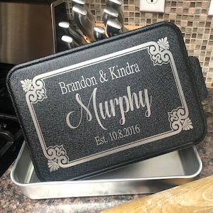 May include: Black rectangular baking pan with a decorative silver border and the engraved names "Brandon & Kindra Murphy" and the date "Est. 10.8.2016". The pan is resting inside a silver metal baking sheet.