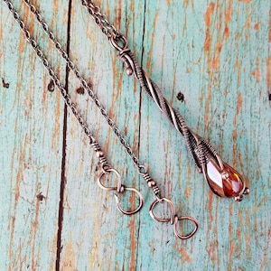 May include: A copper necklace with a twisted wire pendant and a clear amber stone. The necklace has a lobster clasp closure.