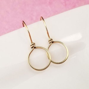 Puede incluir: Un par de pendientes de aro de oro con un diseño simple y minimalista. Los pendientes están hechos de alambre fino y tienen una forma circular delicada.