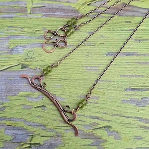 May include: A copper necklace with a coiled wire design and green gemstone beads. The necklace has a simple chain and a clasp.