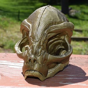 May include: A gold-colored 3D printed alien skull with detailed features and a textured surface.