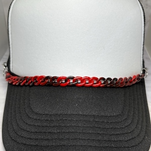 May include: A black and white trucker hat with a red and brown chain across the front. The hat has a white front panel and a black brim. The chain is made of plastic links.