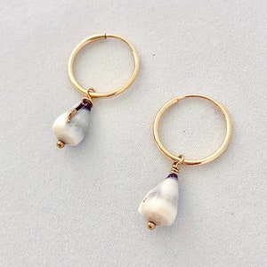 May include: A pair of gold hoop earrings, each with a teardrop-shaped pendant. The pendants are white with gray and brown marbling, and a small gold bead at the bottom. The earrings are displayed on a light gray surface.