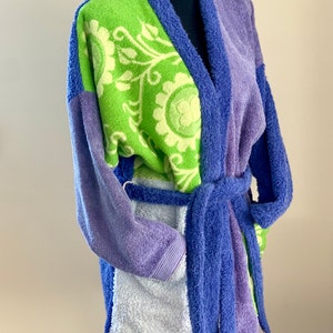May include: A patchwork robe with a green floral pattern on the front, a purple and blue striped pattern on the back, and a light blue trim. The robe has a tie belt.