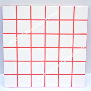 May include: A square, white tile surface with a grid of red lines. The grid divides the surface into smaller, equal squares. The red lines are evenly spaced and create a symmetrical pattern.