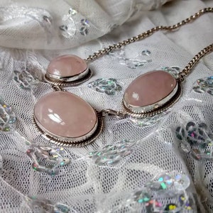 Pu&ograve; includere: Una collana a catena d'argento con tre pietre di quarzo rosa di forma ovale. Le pietre sono incastonate in castoni d'argento e sono collegate da una catena d'argento.