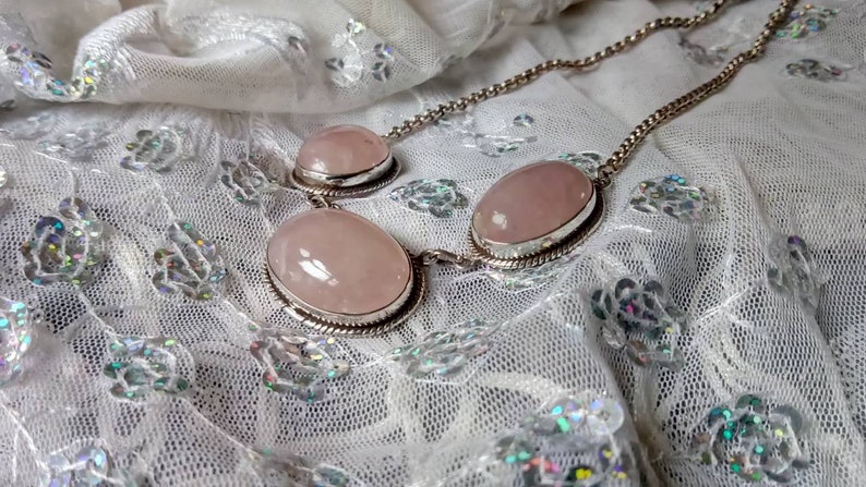 Pu&ograve; includere: Una collana a catena d'argento con tre pietre di quarzo rosa di forma ovale. Le pietre sono incastonate in castoni d'argento e sono collegate da una catena d'argento.
