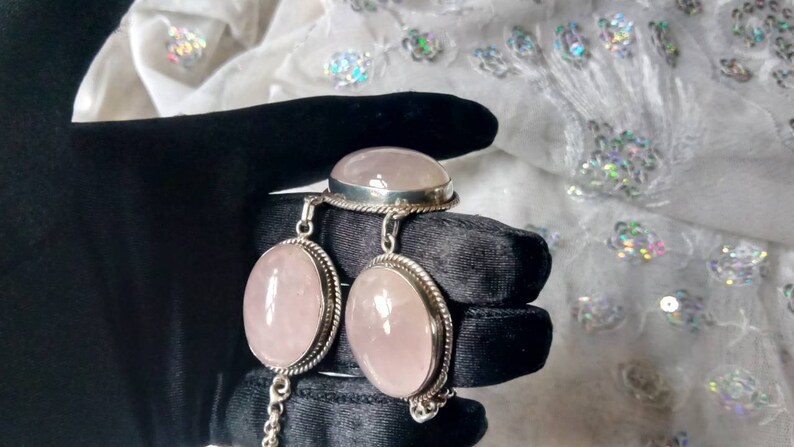 Pu&ograve; includere: Un set di gioielli in quarzo rosa con un anello, un braccialetto e un paio di orecchini. I gioielli sono in argento sterling e presentano pietre di quarzo rosa di forma ovale.