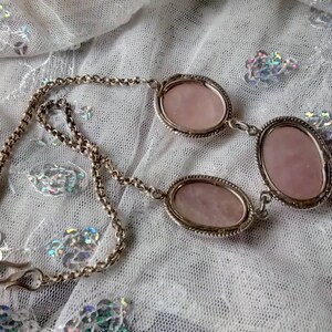 Pu&ograve; includere: Una collana a catena d'argento con tre pietre rosa di forma ovale. Le pietre sono incastonate in castoni d'argento e sono collegate da anelli d'argento.