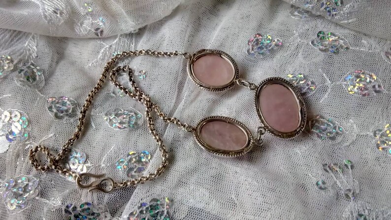 Pu&ograve; includere: Una collana a catena d'argento con tre pietre rosa di forma ovale. Le pietre sono incastonate in castoni d'argento e sono collegate da anelli d'argento.
