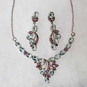 May include: A silver necklace and earrings set with blue and pink gemstones. The necklace features a delicate chain with a pendant that has a cluster of blue and pink gemstones. The earrings are drop earrings with a similar design.