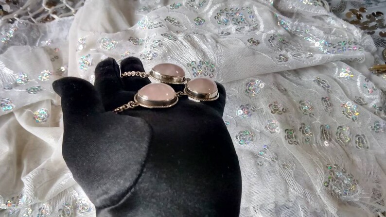 Pu&ograve; includere: Un braccialetto d'argento con tre pietre ovali rosa. Il braccialetto &egrave; su una superficie nera.