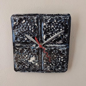 May include: A black and white clock with a red second hand. The clock face is made of a textured material that looks like tin.