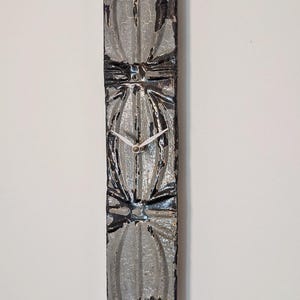 May include: A grey and black clock with a distressed finish. The clock face is made of a patterned metal with a white clock hand.