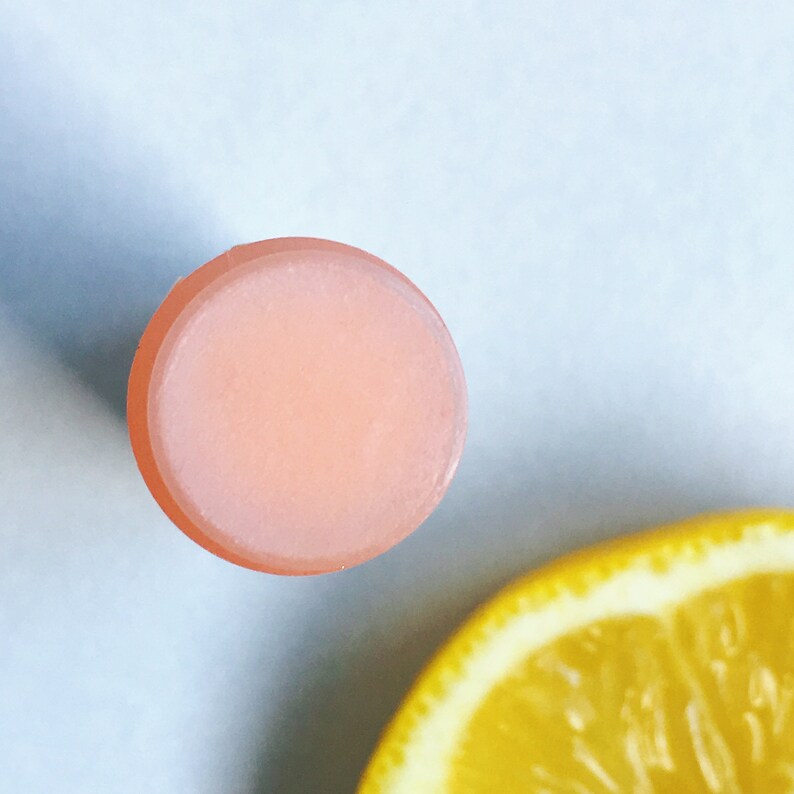 May include: A close-up of a pink lip balm stick. The balm is smooth and shiny, and the stick is round.