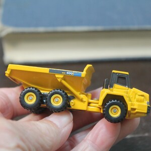 Pode incluir: Um cami&atilde;o basculante de brinquedo amarelo com pneus pretos e uma cabine preta. O cami&atilde;o tem o n&uacute;mero "400" impresso na lateral. O brinquedo &eacute; segurado em uma m&atilde;o.