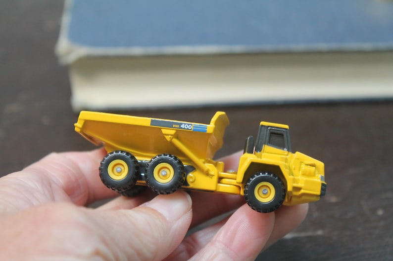 Pode incluir: Um cami&atilde;o basculante de brinquedo amarelo com pneus pretos e uma cabine preta. O cami&atilde;o tem o n&uacute;mero "400" impresso na lateral. O brinquedo &eacute; segurado em uma m&atilde;o.